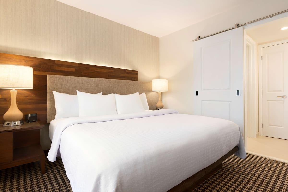 A neatly made bed with white linens, a wooden headboard, and two bedside lamps.