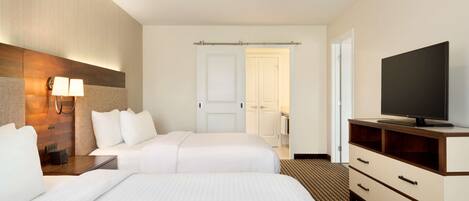 A hotel room with two beds, a TV, a ceiling fan, and a bathroom door.