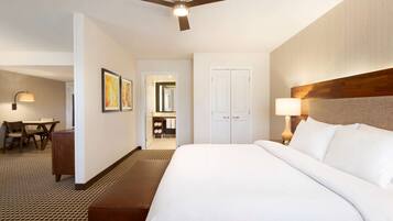 A hotel room with a large bed, a desk, a chair, a ceiling fan, and a bathroom visible through an open door.