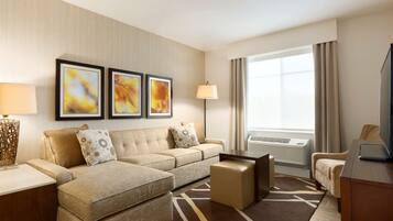 A modern hotel room with a sofa set, a coffee table, a TV, and artwork on the wall.