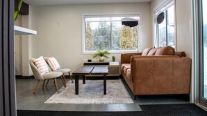 A living room with a sofa, a chair, a coffee table, a potted plant, and a window with a view of trees. - Super 8 by Wyndham Clearwater BC (Clearwater)
