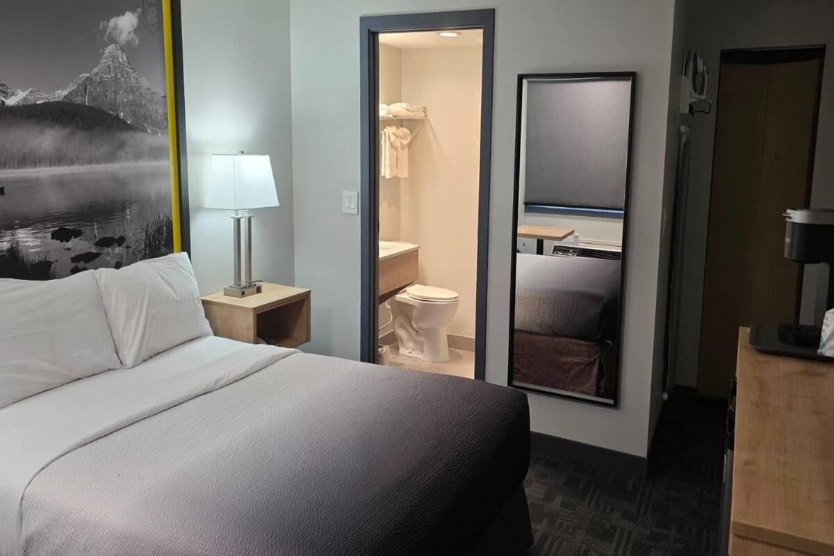 A hotel room with a bed, a bathroom, a desk, and a mirror.