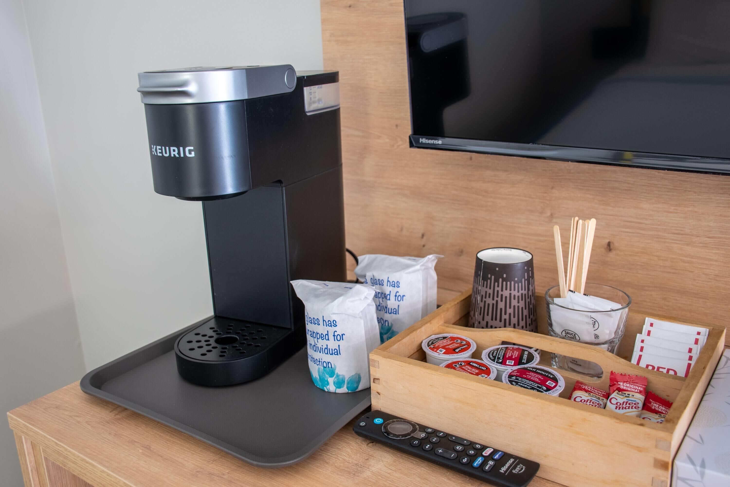 A coffee maker, a tray, a remote control, a tray of coffee pods, and a mug with a spoon.