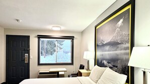 A hotel room with a bed, a desk, a chair, a lamp, a window with a view of snow-covered trees, and a framed picture on the wall. - Super 8 by Wyndham Clearwater BC (Clearwater)