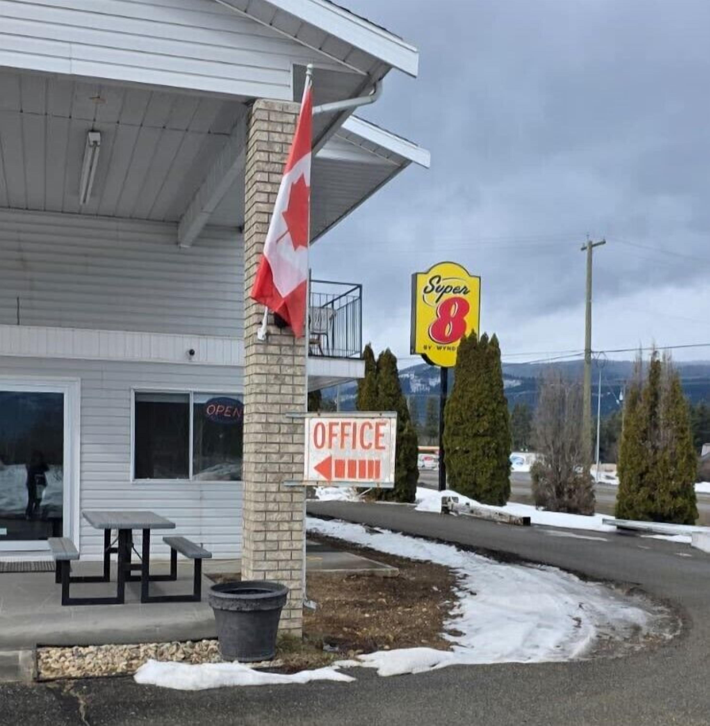 Un motel Super 8 con una bandera, un letrero de la oficina y vistas a las montañas.