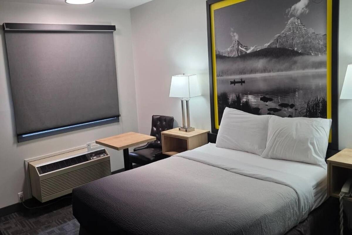 A hotel room with a bed, a desk, a chair, a lamp, a heater, and a large framed picture on the wall.