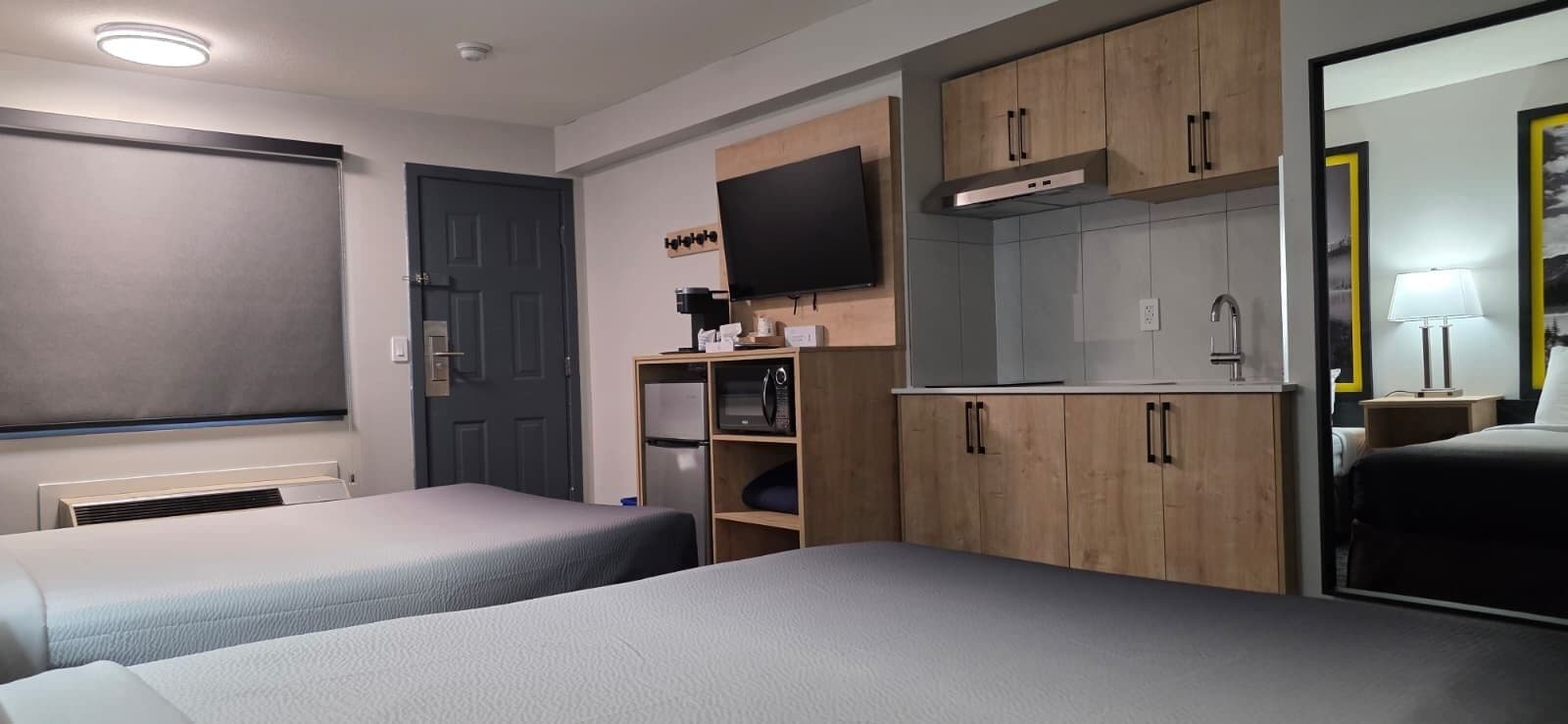 Ein Hotelzimmer mit zwei Betten, einem Fernseher, einer Küchenzeile und einem Badezimmer.