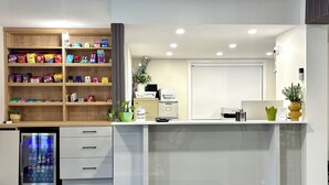 A reception desk with a glass partition, a refrigerator with Pepsi products, and a shelf with snacks. - Super 8 by Wyndham Clearwater BC (Clearwater)
