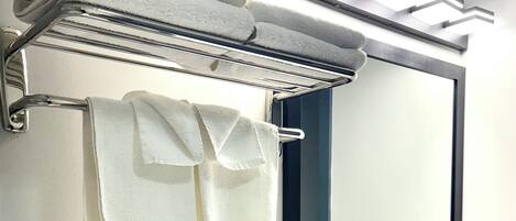 A bathroom with a towel rack holding folded towels, a mirror, and a wall-mounted light fixture.