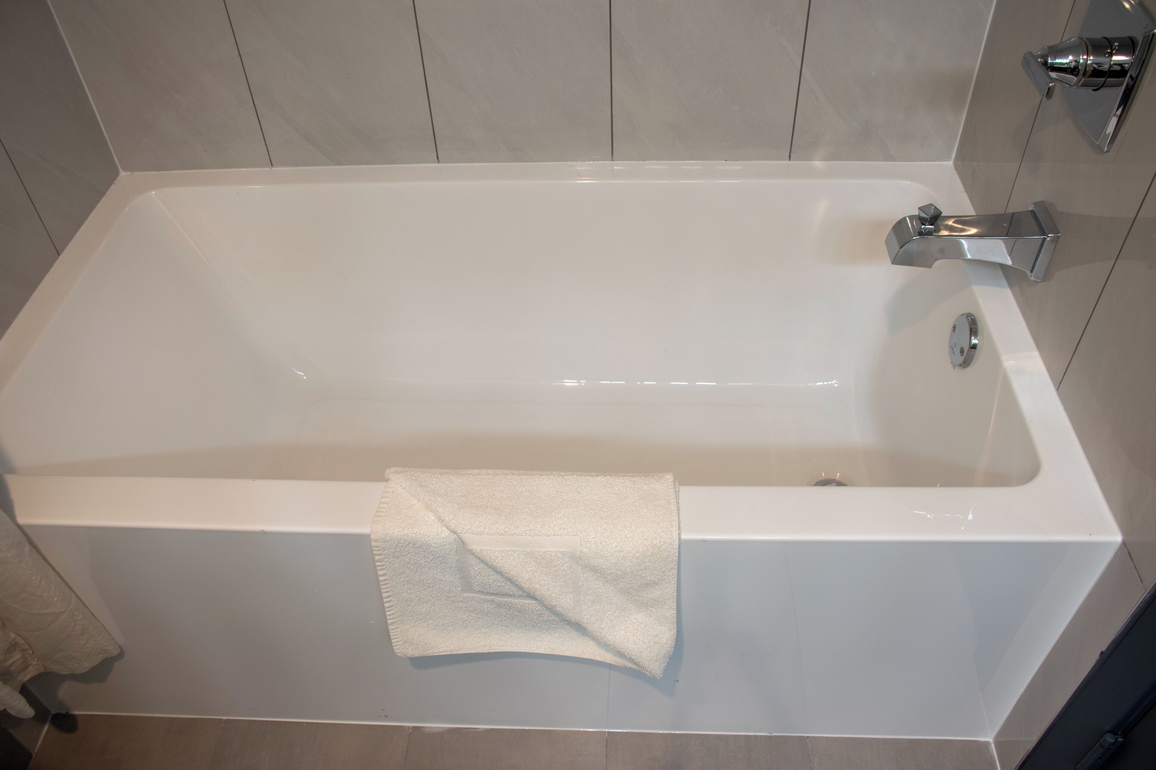 A white bathtub with a towel, a chrome faucet, and a wall-mounted control panel.