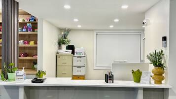 A reception desk with a white counter, a filing cabinet, a small plant, a digital clock, and a whiteboard on the wall.