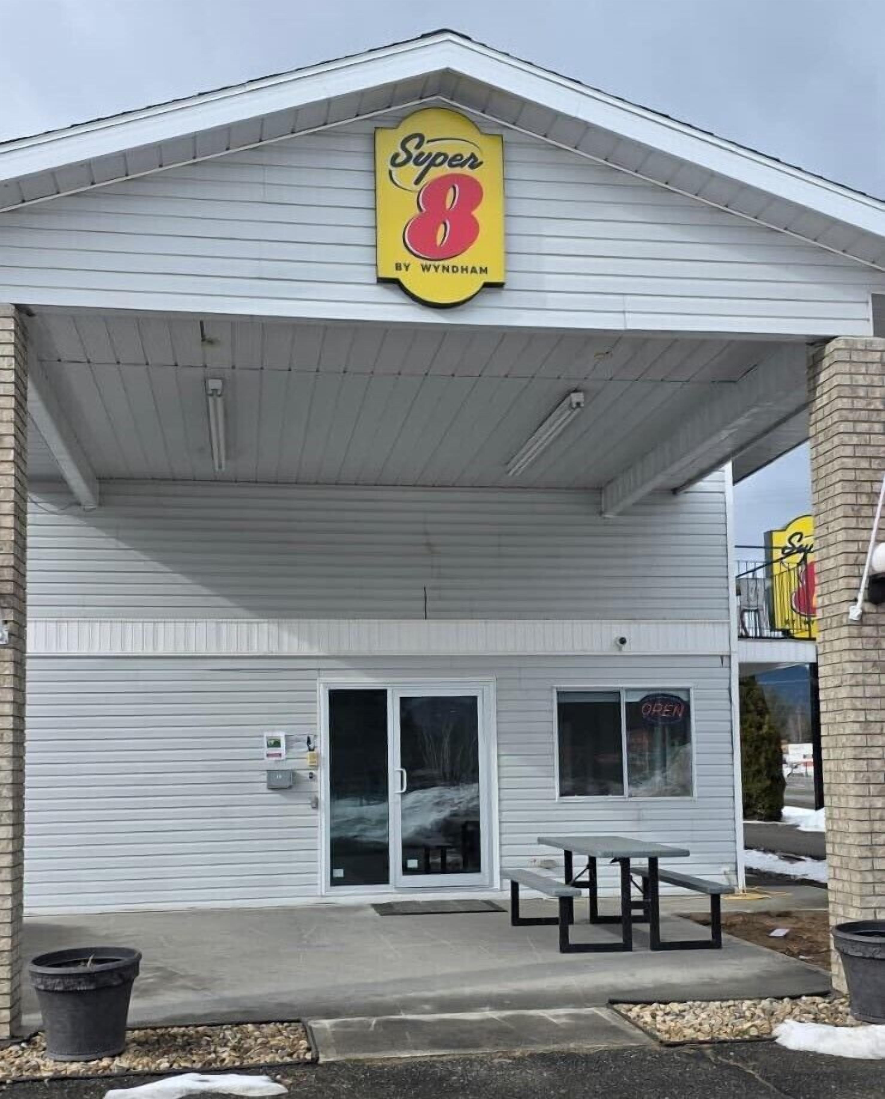 A Super 8 motel with a covered entrance, a patio table, and a sign indicating the name and location.
