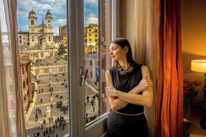 A person standing by a window with a view of a historic building and a staircase.