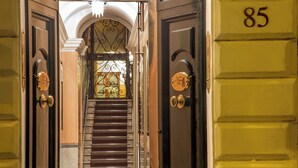 Entrada de un hotel con una escalera, puertas dobles y el número 85 en la pared.