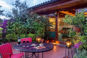 A patio with a round table, red chairs, wine glasses, a bottle of wine, and a candle.