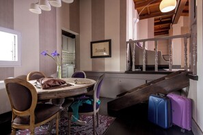 A dining area with a wooden table, chairs, a vase with flowers, and a staircase with luggage.