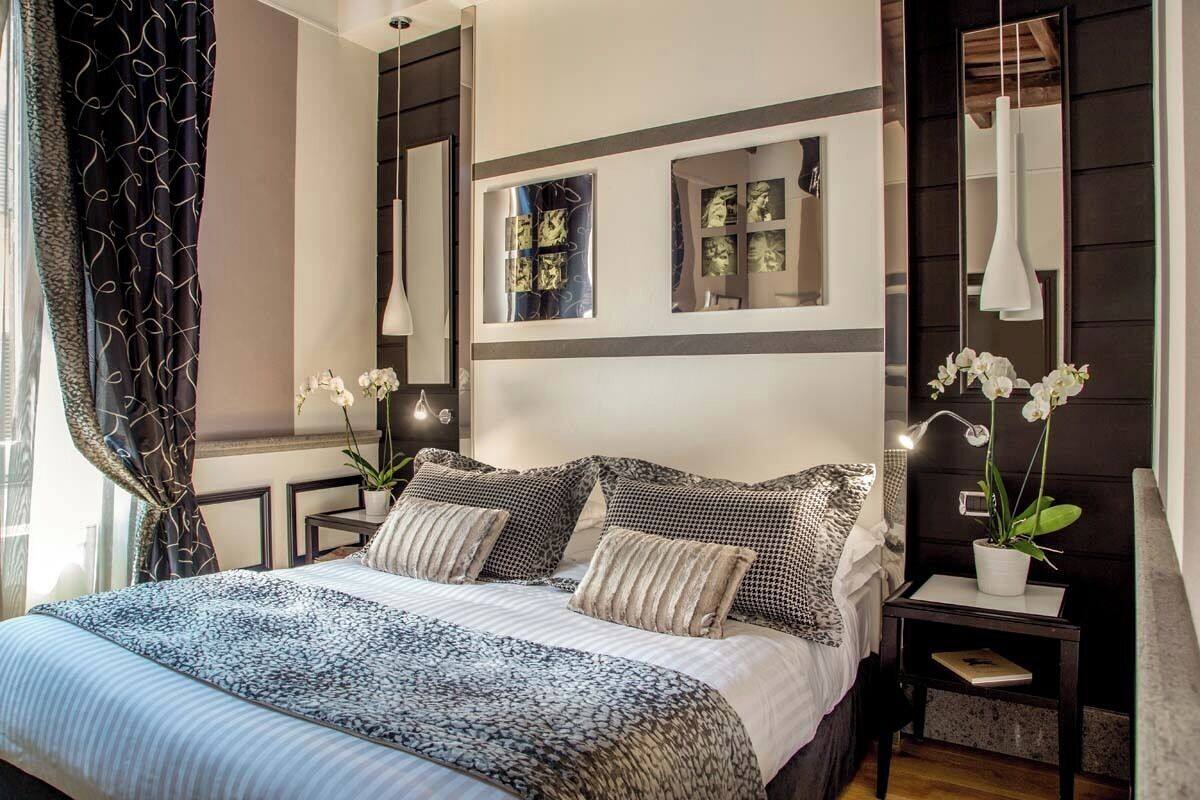 A modern bedroom with a large bed, two bedside tables, a mirror, and a potted plant.