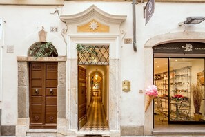 A building entrance with a double door, a hallway leading to a shop, and a sign above the door. - Inn At The Spanish Steps (Rome)