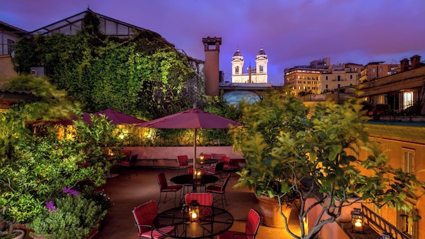 An outdoor patio with tables and chairs, surrounded by greenery and potted plants.