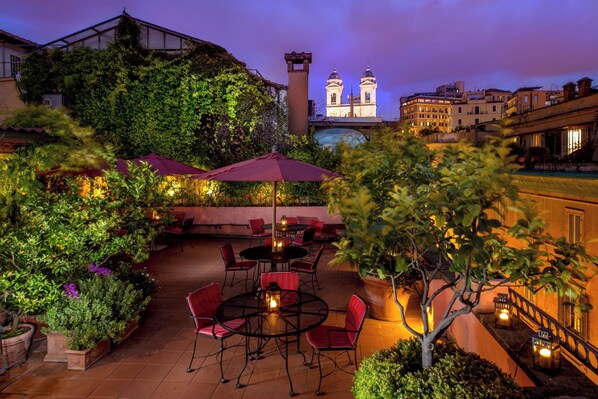 An outdoor patio with tables and chairs, surrounded by greenery and potted plants. - Inn At The Spanish Steps (Rome)