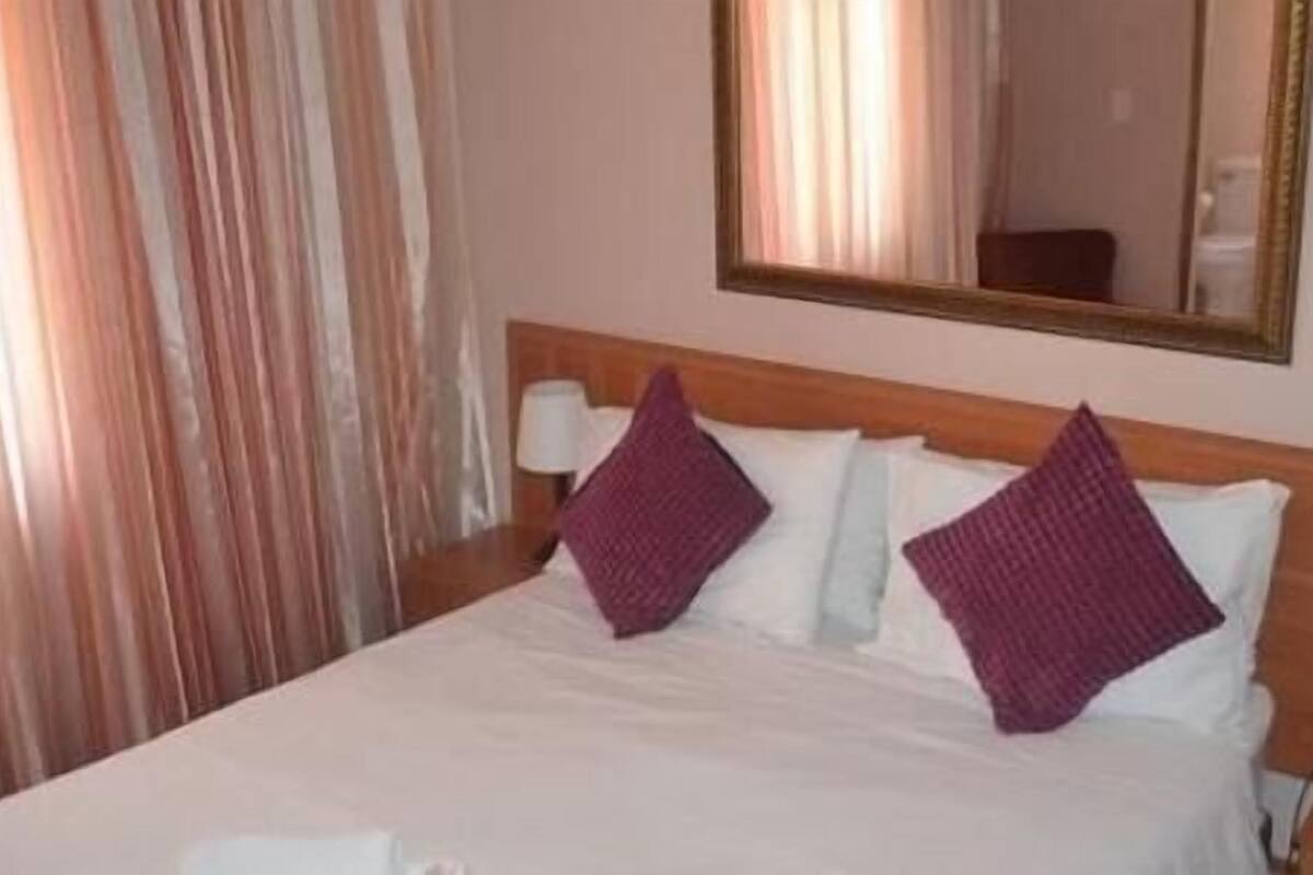 A hotel room with a bed, two pillows, a nightstand with a lamp, and a mirror on the wall.