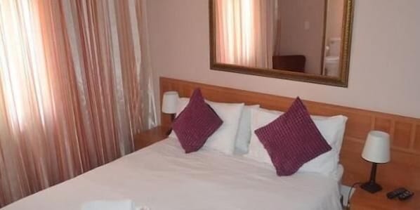 Una habitación de hotel con una cama, dos almohadas, una mesita de noche con lámpara y un espejo en la pared.