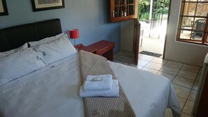 Una cama bien hecha con sábanas blancas, una lámpara de noche roja y un banco de madera.