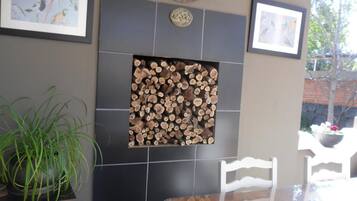 Un área de comedor con pared de azulejos, chimenea con leña, cuadros enmarcados y planta en maceta.