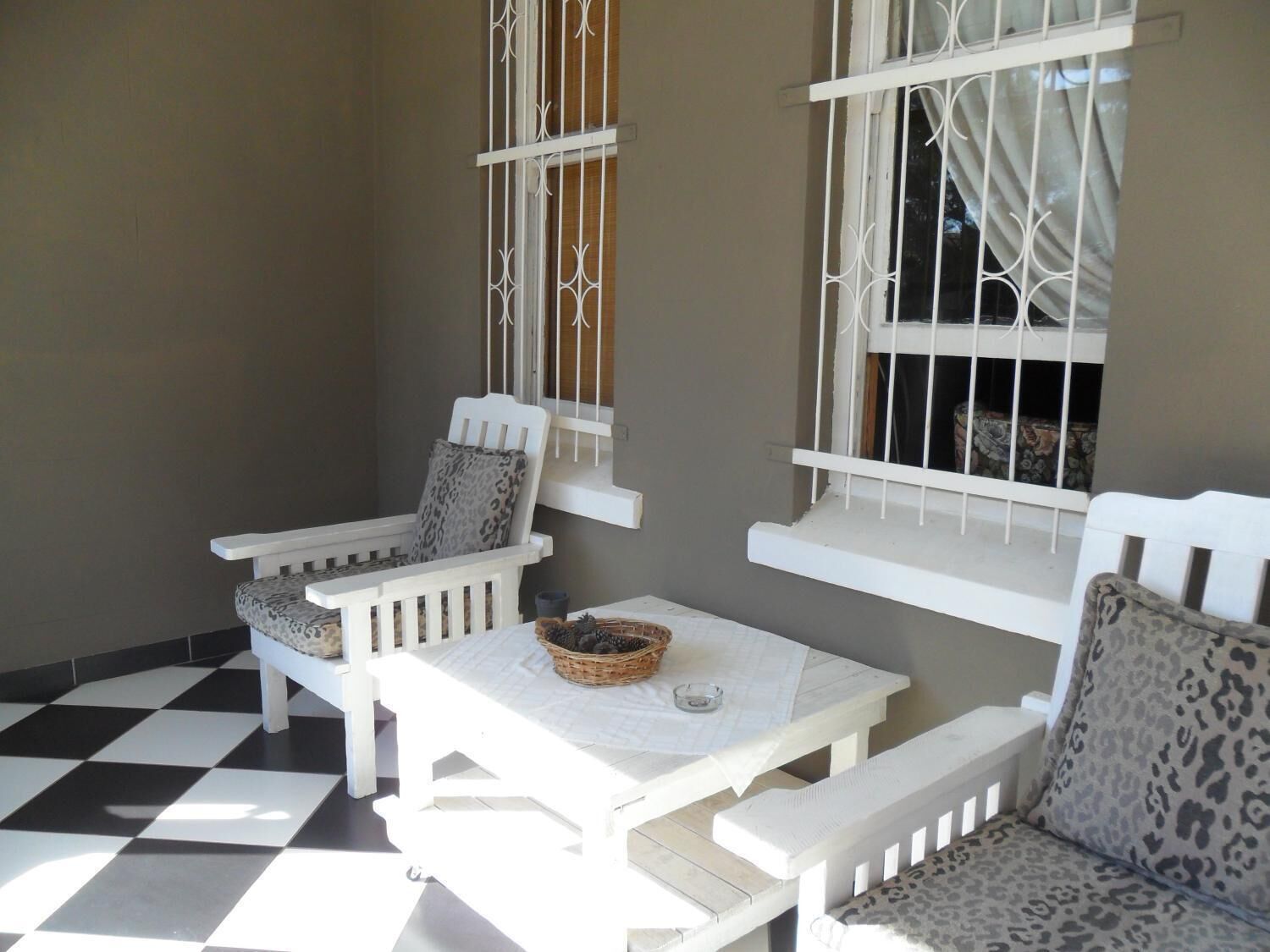 A small, enclosed patio area with a checkered floor, white furniture, and barred windows.