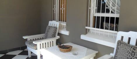 A small, enclosed patio area with a checkered floor, white furniture, and barred windows.