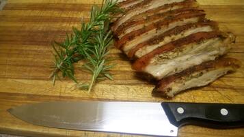 Une planche à découper en bois avec des tranches de viande, une branche de romarin et un couteau.