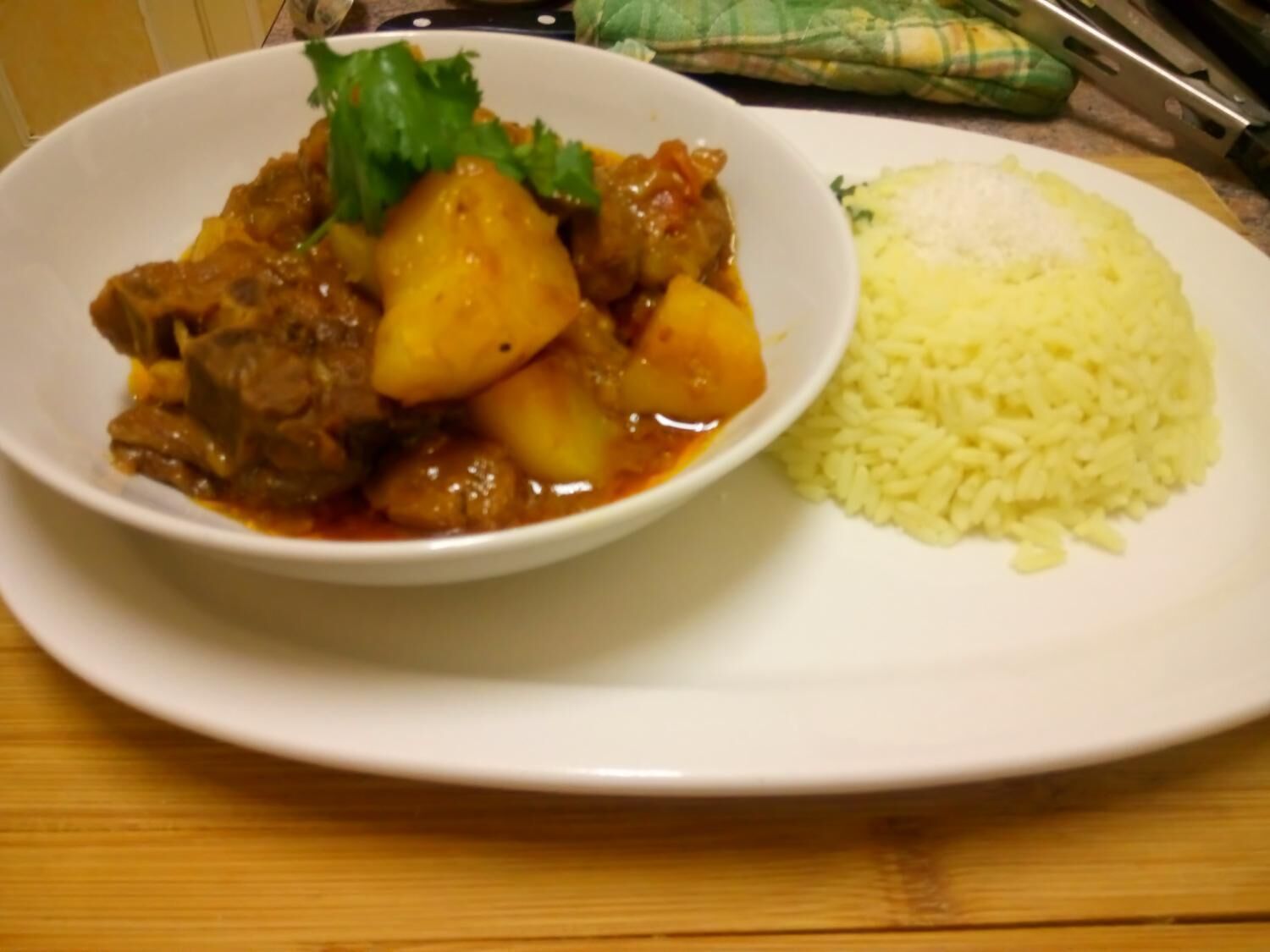 A plate with a meat and potato dish and a side of rice.