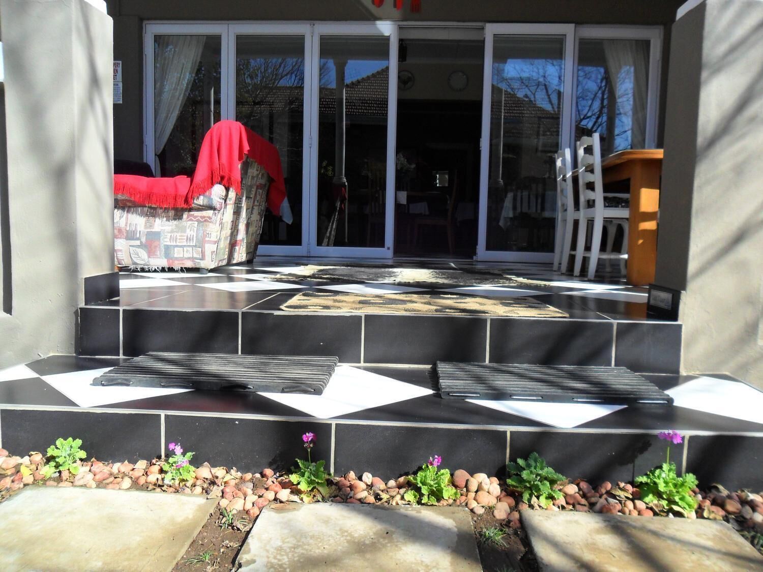 Un juego de escalones exteriores que conducen a la entrada de un edificio con puerta de vidrio, un paño rojo cubriendo una silla y una escalera apoyada contra la pared.