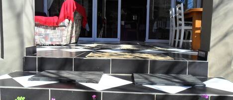 Un juego de escalones exteriores que conducen a la entrada de un edificio con puerta de vidrio, un paño rojo cubriendo una silla y una escalera apoyada contra la pared.