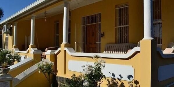 Un edificio amarillo con un porche cubierto, columnas y una escalera que lleva a la entrada.