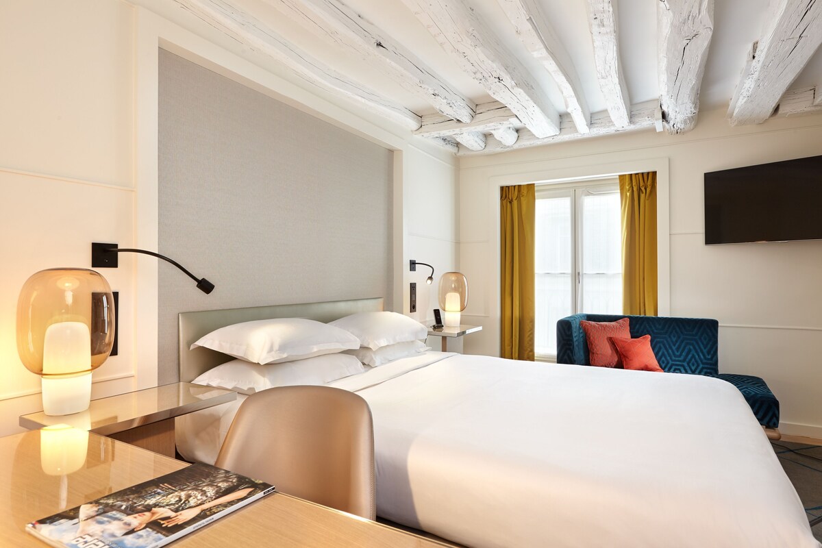 Camera d'albergo con un letto, comodino, lampada, sedia e televisore a parete.