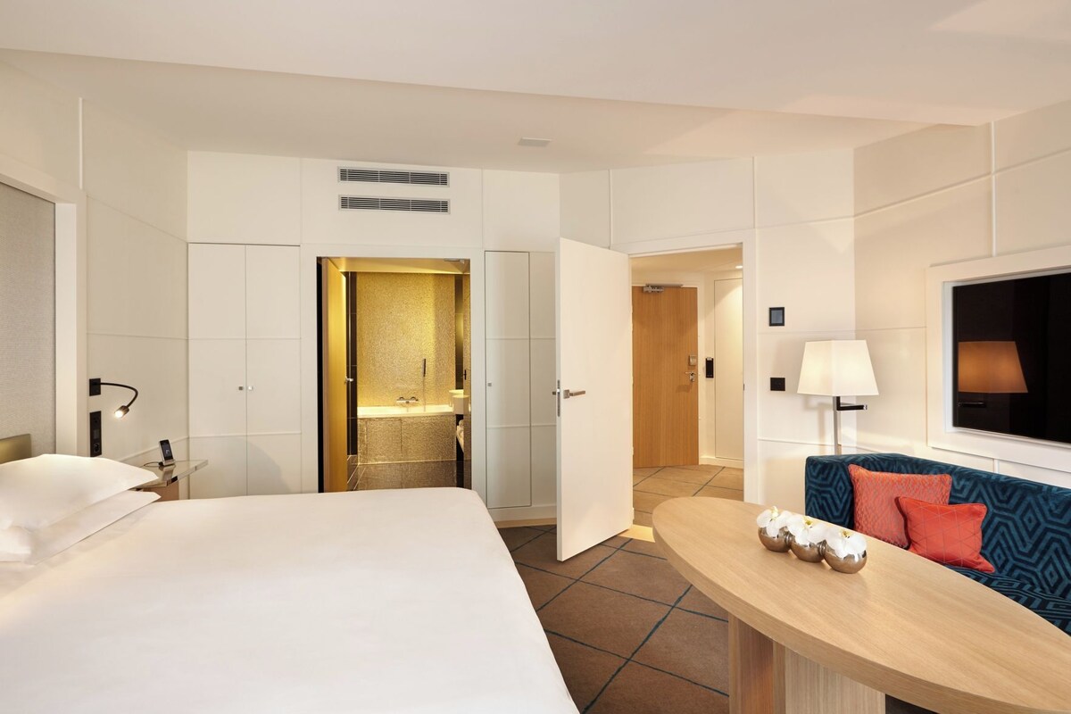 Una camera d'albergo con un letto, una scrivania, un bagno con doccia e una TV fissata al muro.