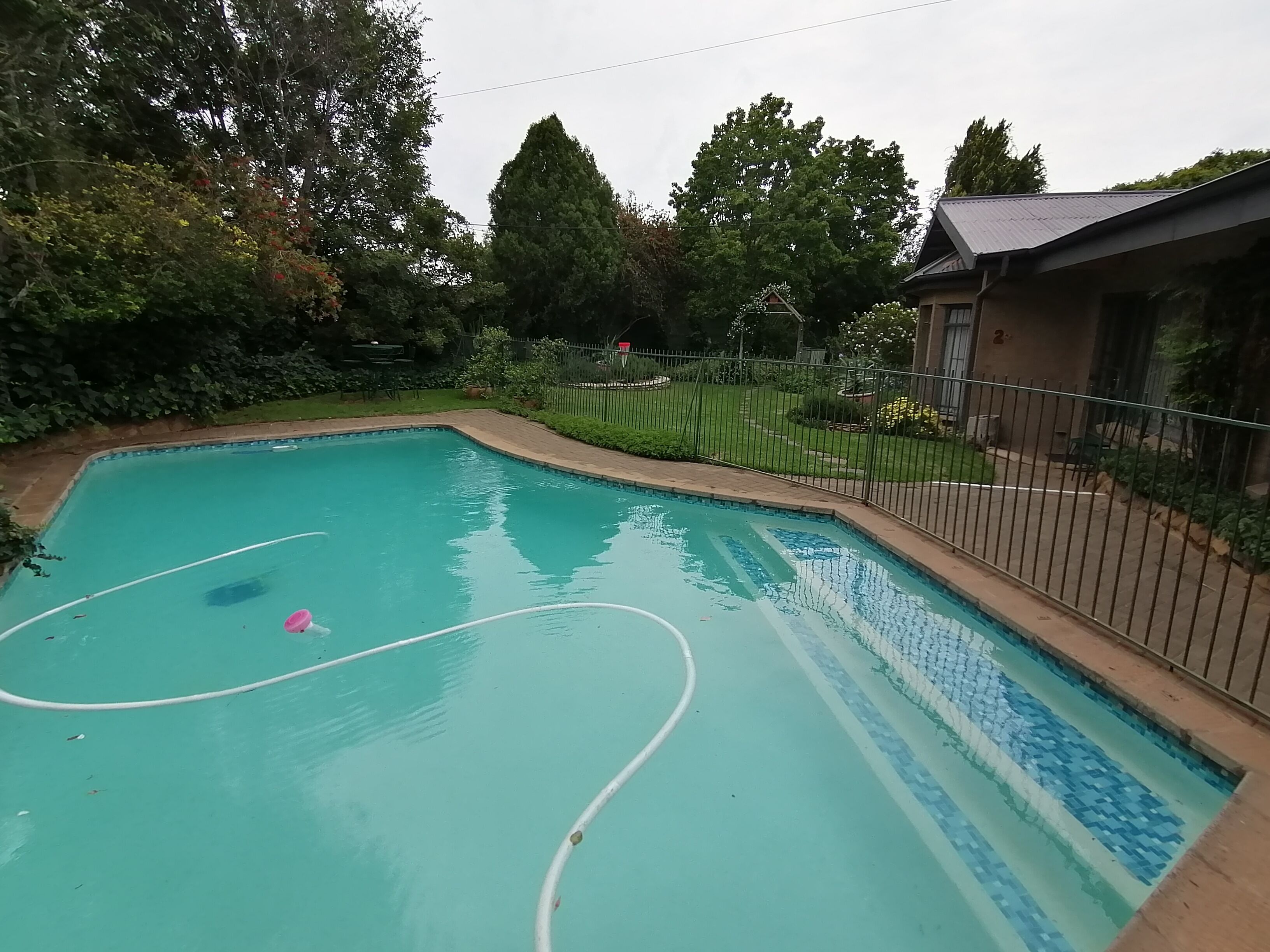 A swimming pool with a tiled edge, surrounded by a fence and greenery.