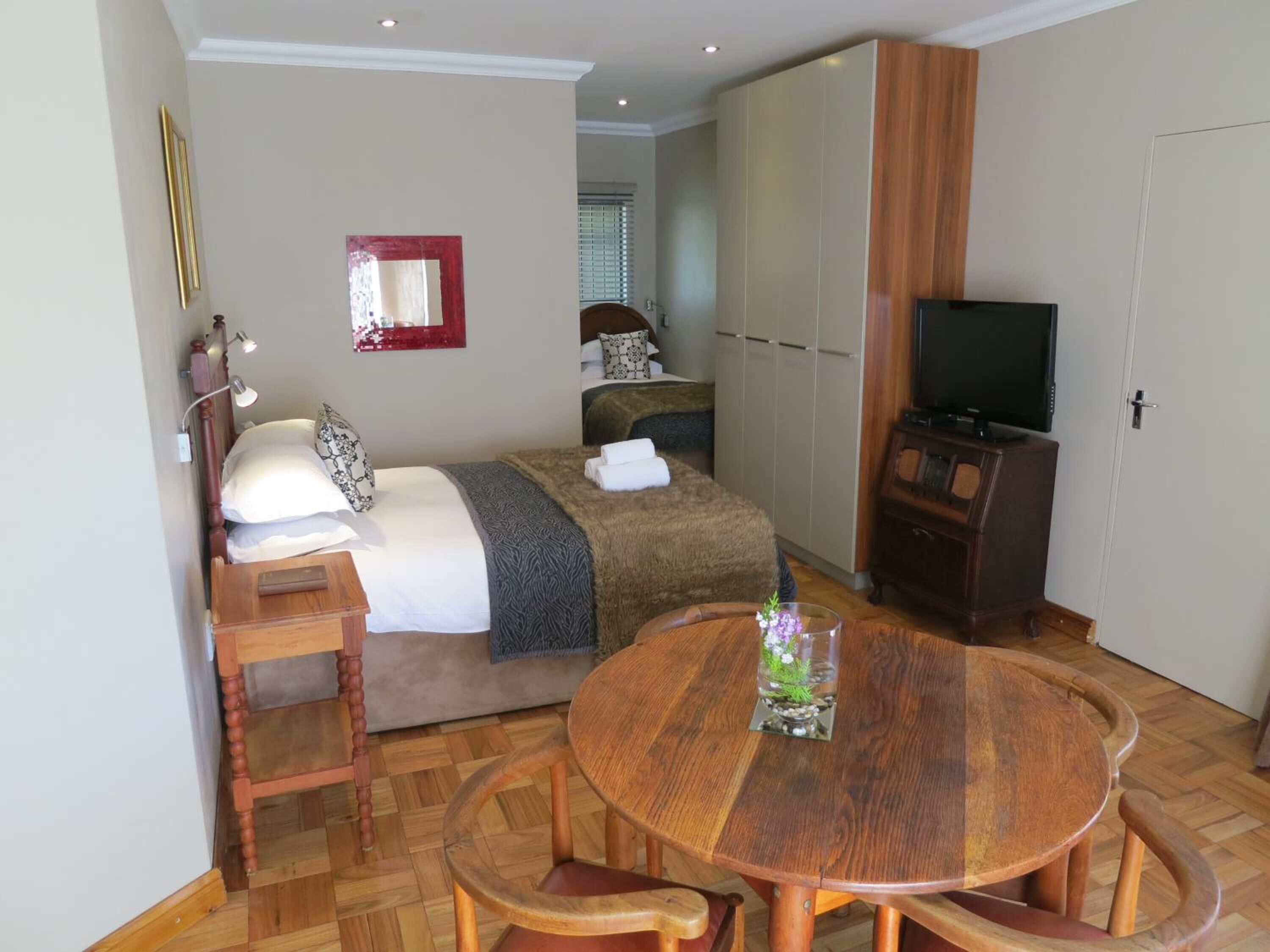 A hotel room with a bed, a TV, a wardrobe, and a dining table with chairs.