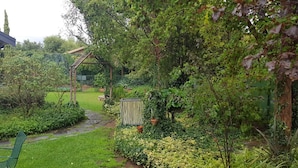 En have med et træbeklædt pergola, en murstensbygning og en sti.