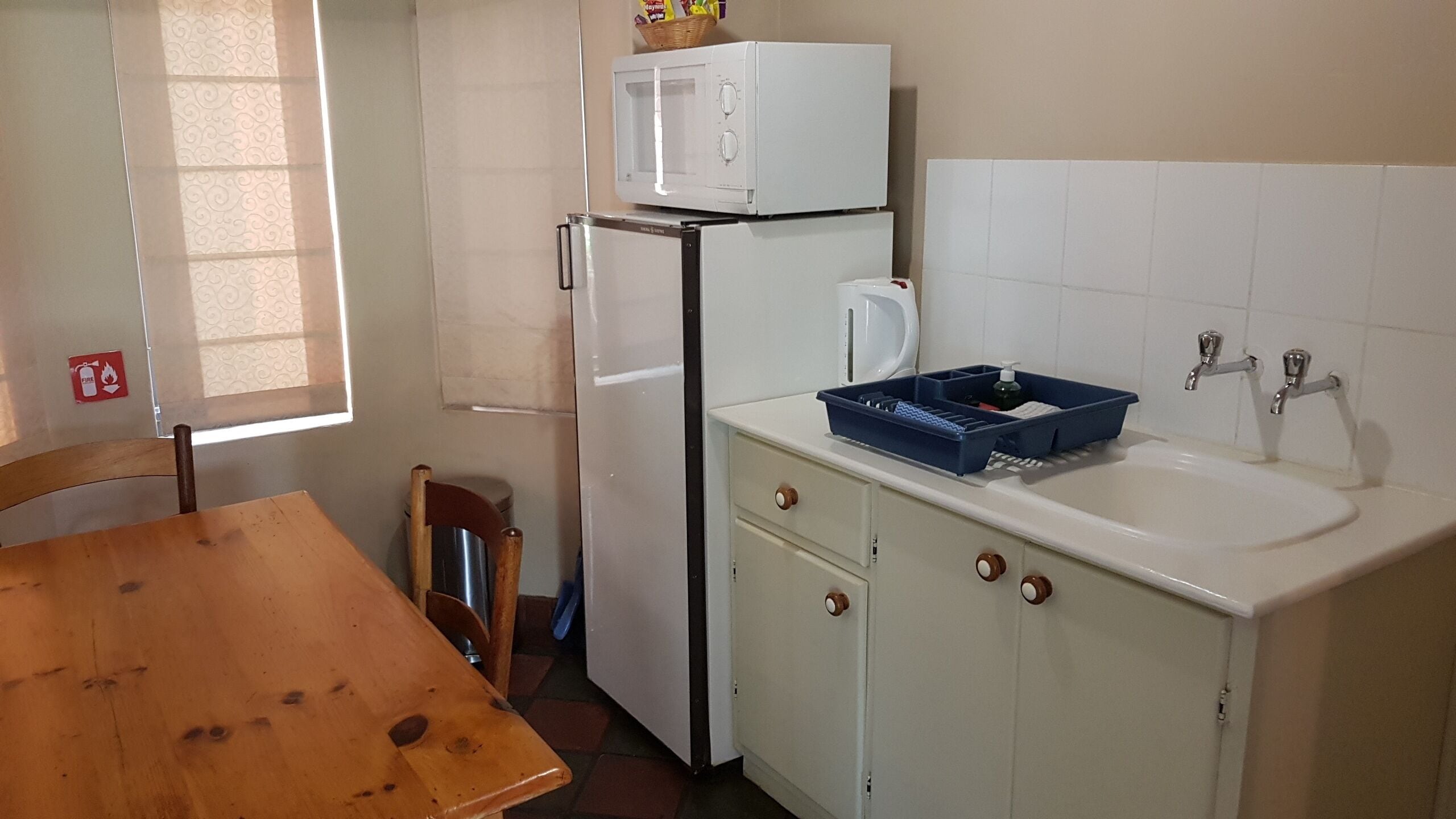 Cocina compacta con refrigerador, microondas, pileta y una mesa de madera.