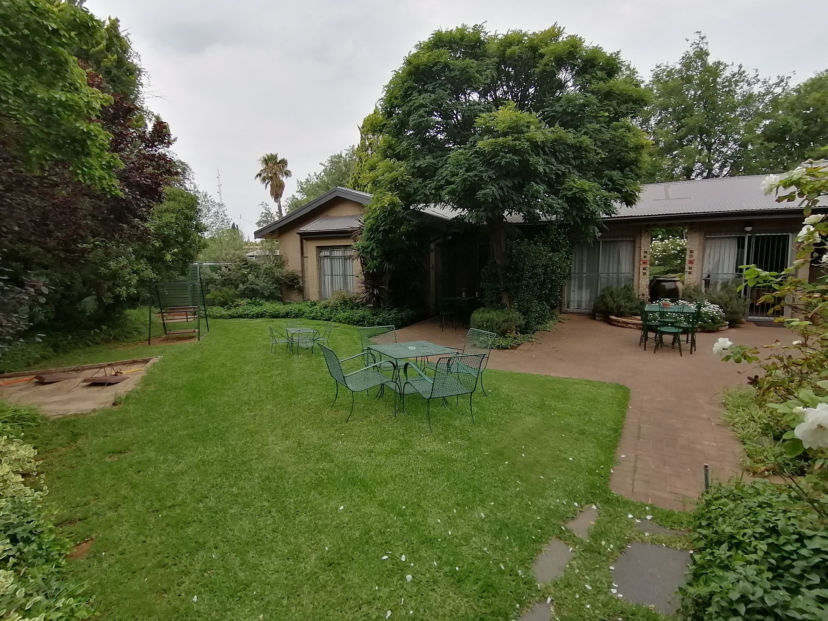 Un patio trasero bien cuidado con césped, una zona de patio con mesas y sillas, y una variedad de plantas y árboles.