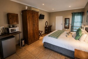 A bedroom with a bed, a desk with a microwave, a wardrobe, a television, and a bathroom. - Lombok Lodge (Port Shepstone)