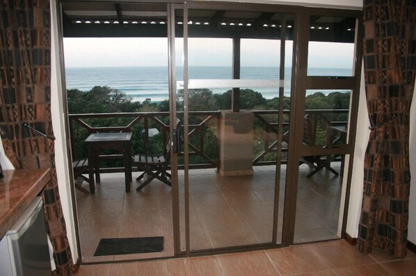 A balcony with a view of the ocean, a table, and chairs.