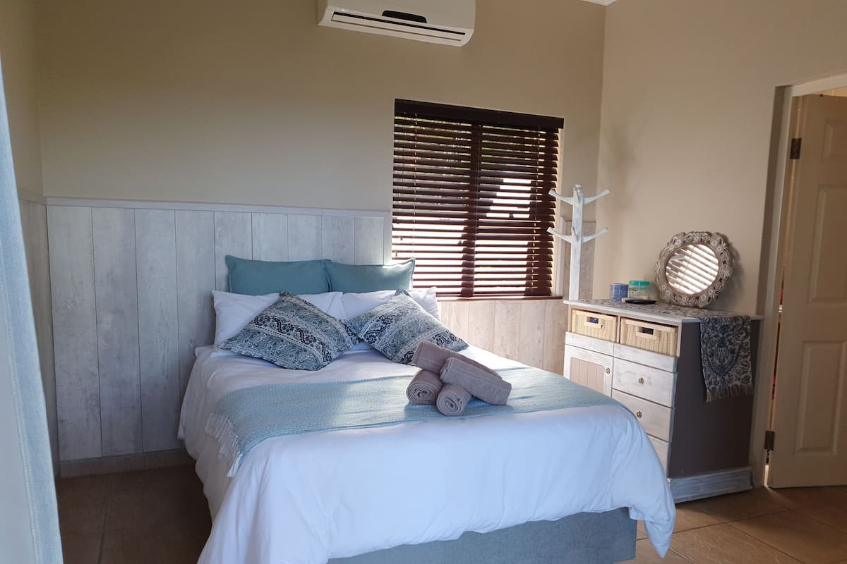 A bedroom with a bed, a dresser, a mirror, and a window with blinds.