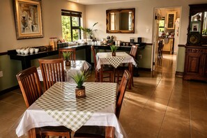 A dining area with a checkered tablecloth, wooden chairs, and a potted plant. - Lombok Lodge (Port Shepstone)