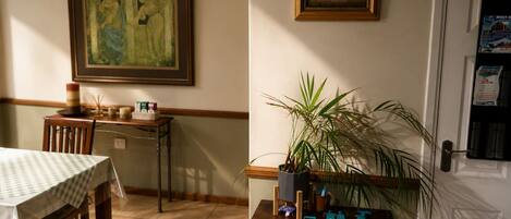 A dining area with a table, chairs, a potted plant, and a wall with framed artwork.