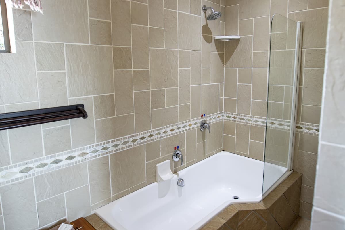 A bathroom with a bathtub, a shower, and a small wooden stool with toiletries.