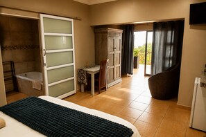 A bedroom with a bed, a bathroom with a bathtub, a dining area with a table and chairs, and a balcony with curtains. - Lombok Lodge (Port Shepstone)