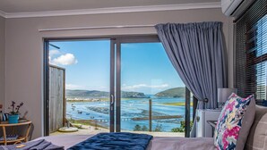 Un dormitorio con un gran ventanal corredera que da a una vista panorámica de la costa.